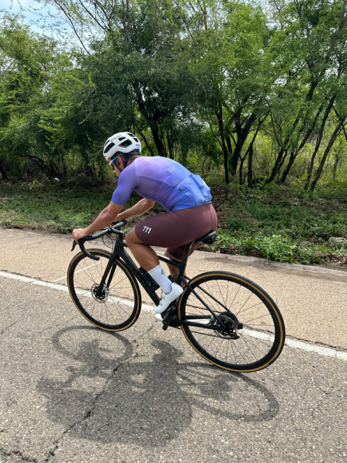 Ciclista entrenando en una bicicleta de ruta, vistiendo el Bib Short sin costura en color terracota de 111 Cientonce. La pantaloneta, diseñada para máximo rendimiento, destaca por su diseño sin costuras y su confección con materiales europeos de alta compresión, ideal para rodadas de larga duración.